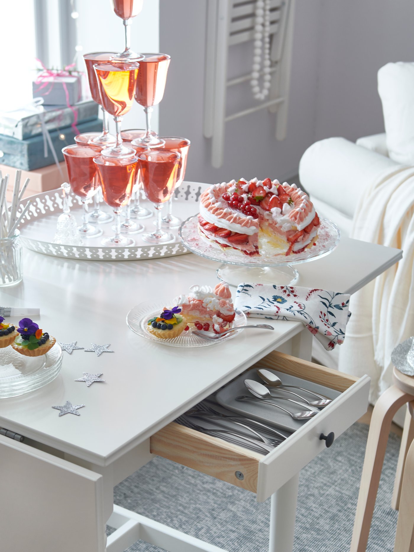 An INGATORP drop-leaf table is filled with party drinks and cakes. A drawer from the table is open to reveal cutleries.