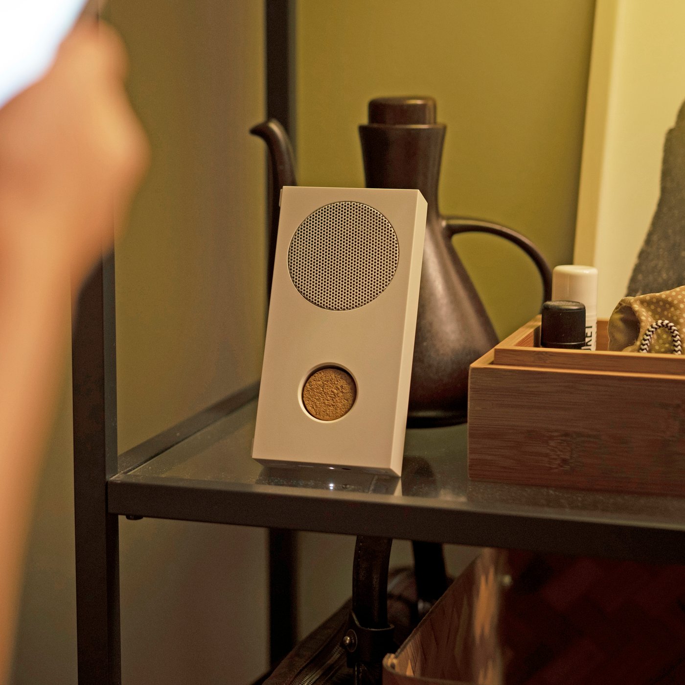 A hand is using a smartphone to turn on an ENEBY portable bluetooth speaker.