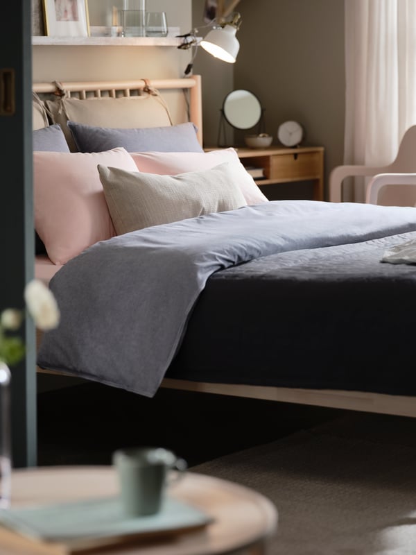 Una recámara con una cama de abedul BJÖRKSNÄS, blancos KOPPARBLAD color azul oscuro, y un escritorio y una silla.