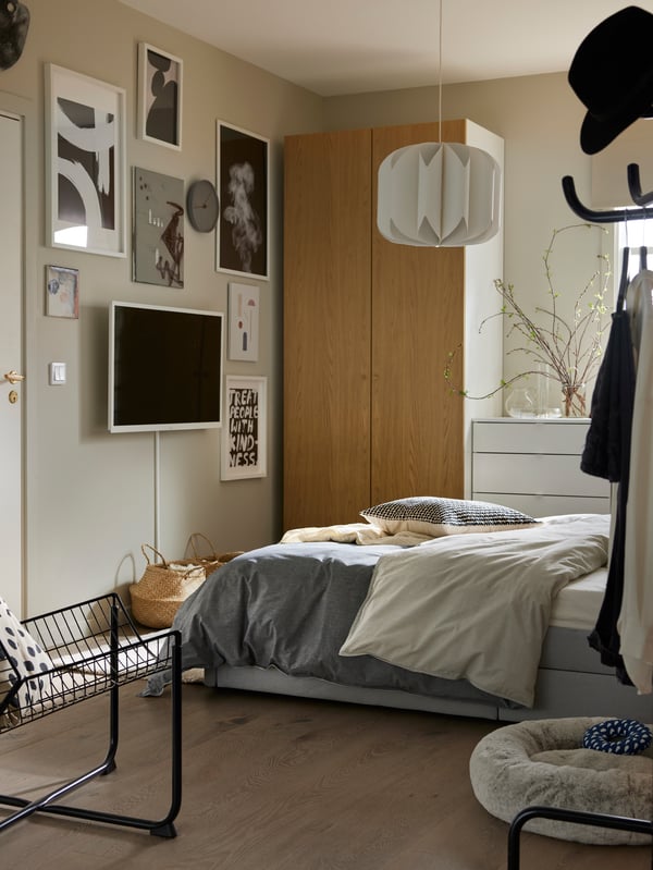 Un letto GLADSTAD grigio con biancheria da letto BLÅVINDA, un guardaroba PAX/STORKLINTA e una parete di quadri di fronte.
