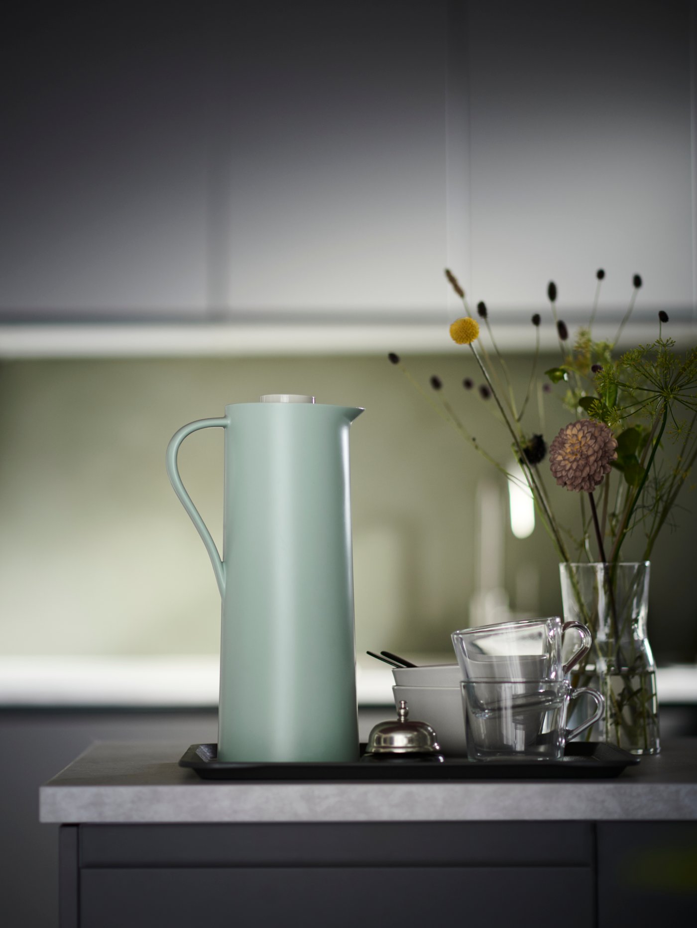 Cocinas con armarios bajos, armarios de pared, encimera, termo, jarrón de cristal con plantas decorativas, taza de cristal, gris bandeja.