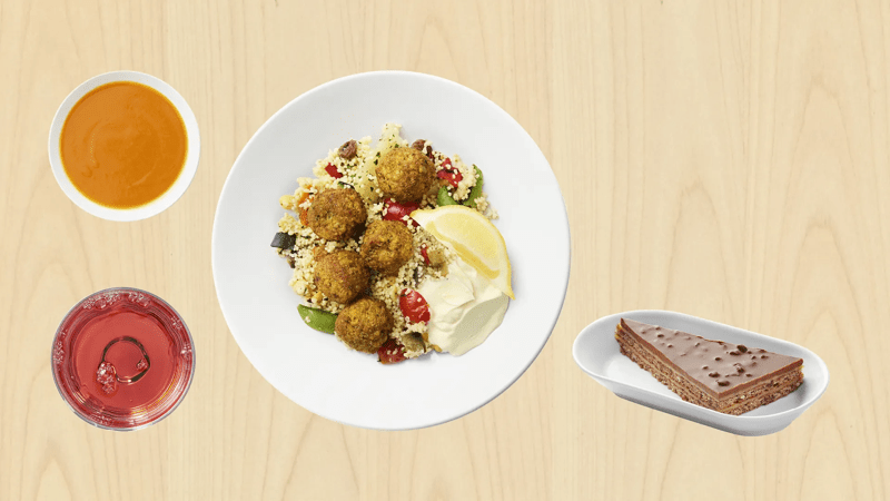 Assiette de falafels avec couscous et citron, accompagnée d’une soupe carotte, d’une boisson rouge et d’un dessert chocolaté.