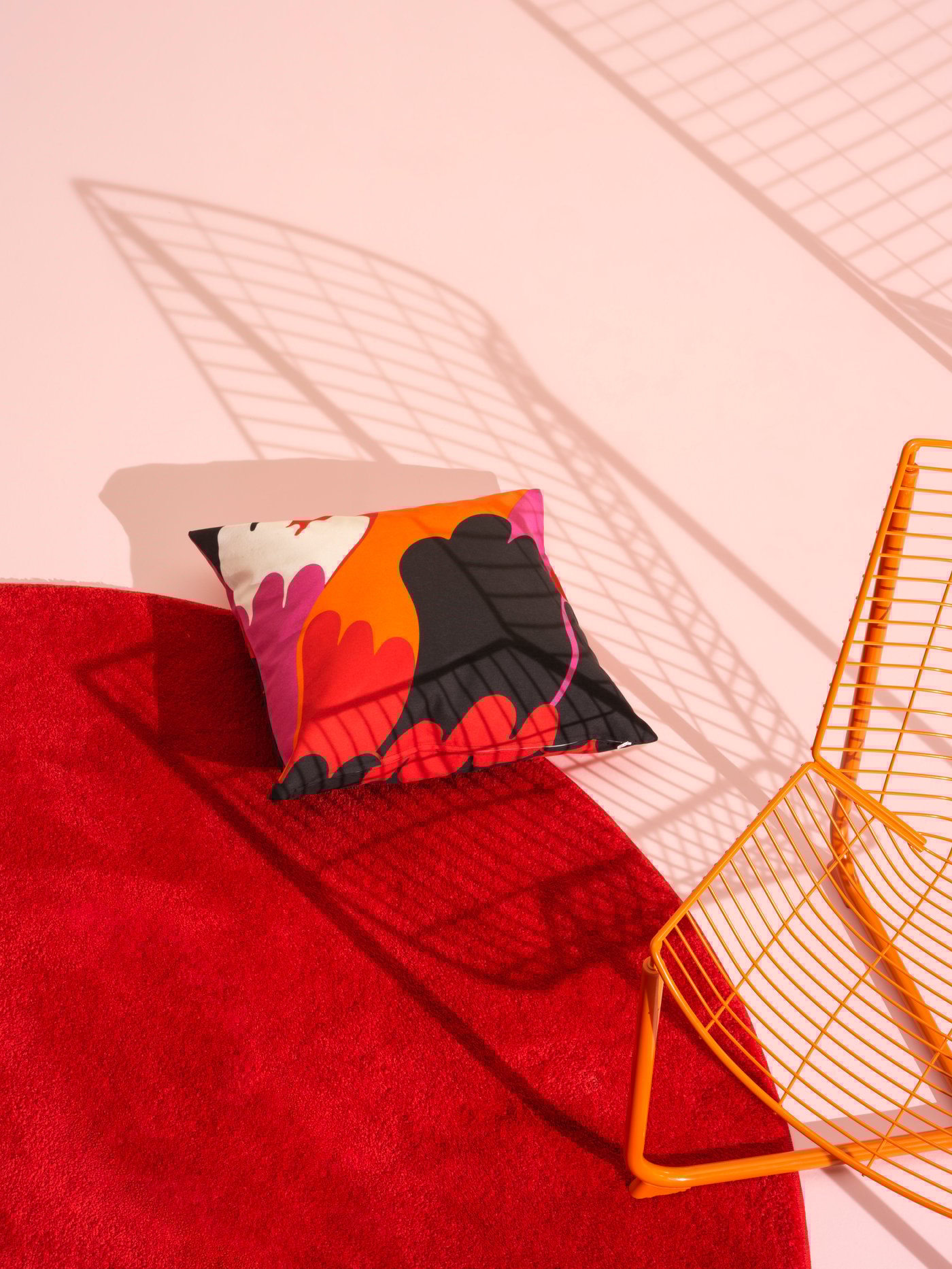 A red circular rug sits on a white floor. A patterned pillow and orange chair sit on top.