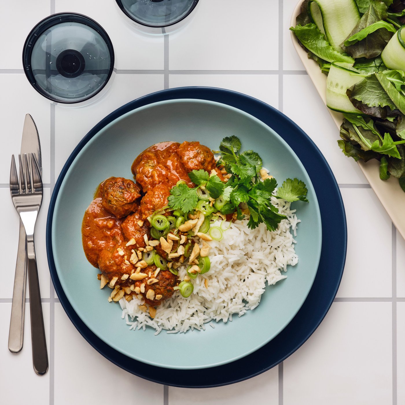 A turquoise plate is placed on top of a blue plate and contains rice and a stew and is garnished with coriander.