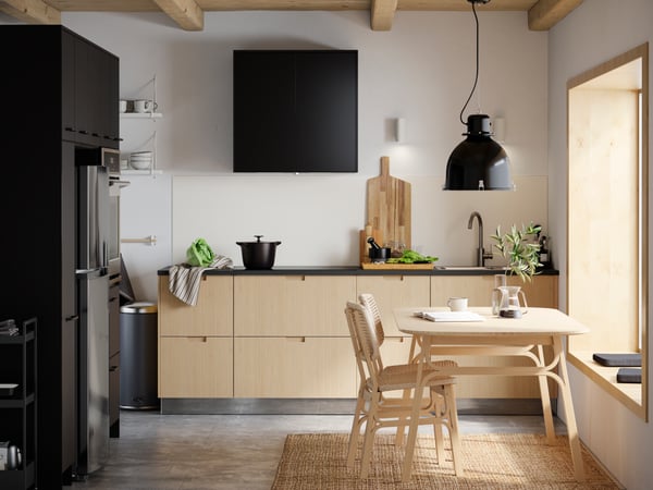 Keuken met VEDHAMN keukenfronten in eikenpatroon, keukenkasten, tafel met stoelen en witte HAVSEN spoelbak.