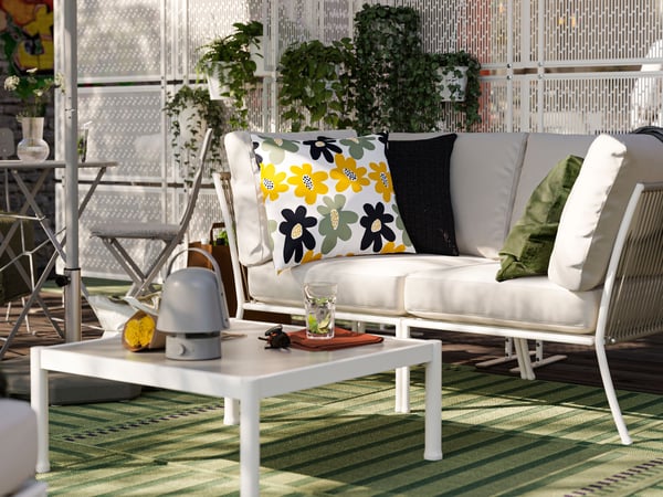 An outdoor lounge area with a two-seat SEGERÖN outdoor sofa and extra cushions. Near it are a cafe table and a coffee table.