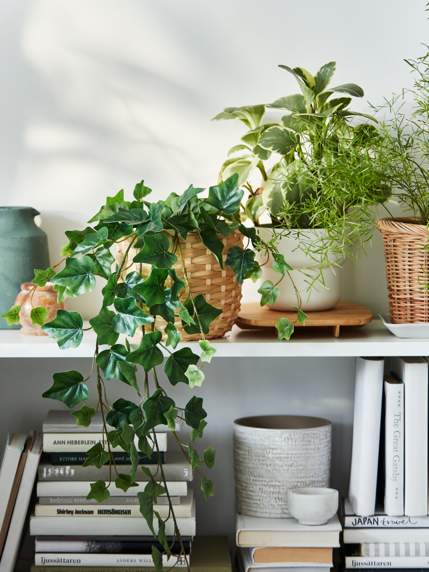 Una sección de una librería BILLY de color blanco llena de una combinación de libros y plantas artificiales FEJKA en maceteros variados.