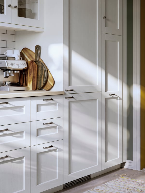 A bright kitchen has a row of base cabinets and wall cabinets with white ENKÖPING fronts and an EKBACKEN worktop.