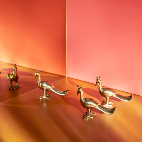 Three golden decorative birds in a bright room facing a mirror.