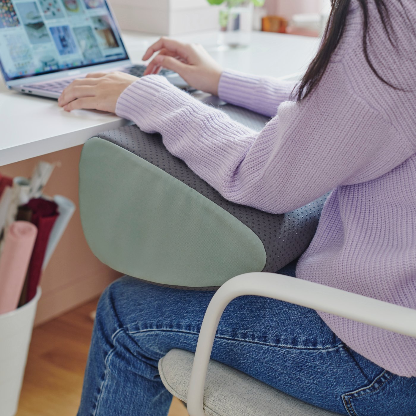 Eine Person sitzt an einem weißen Schreibtisch. Ihre Unterarme ruhen auf einer ergonomischen ÖVNING Mehrzweck-Fußstütze.