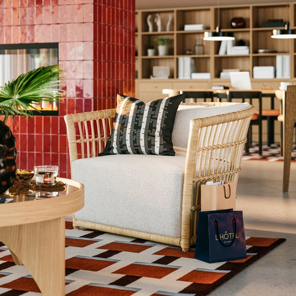 A close-up on STOCKHOLM 2025 grey/white armchair next to a round coffee table in a spacious hotel lobby by a fireplace.