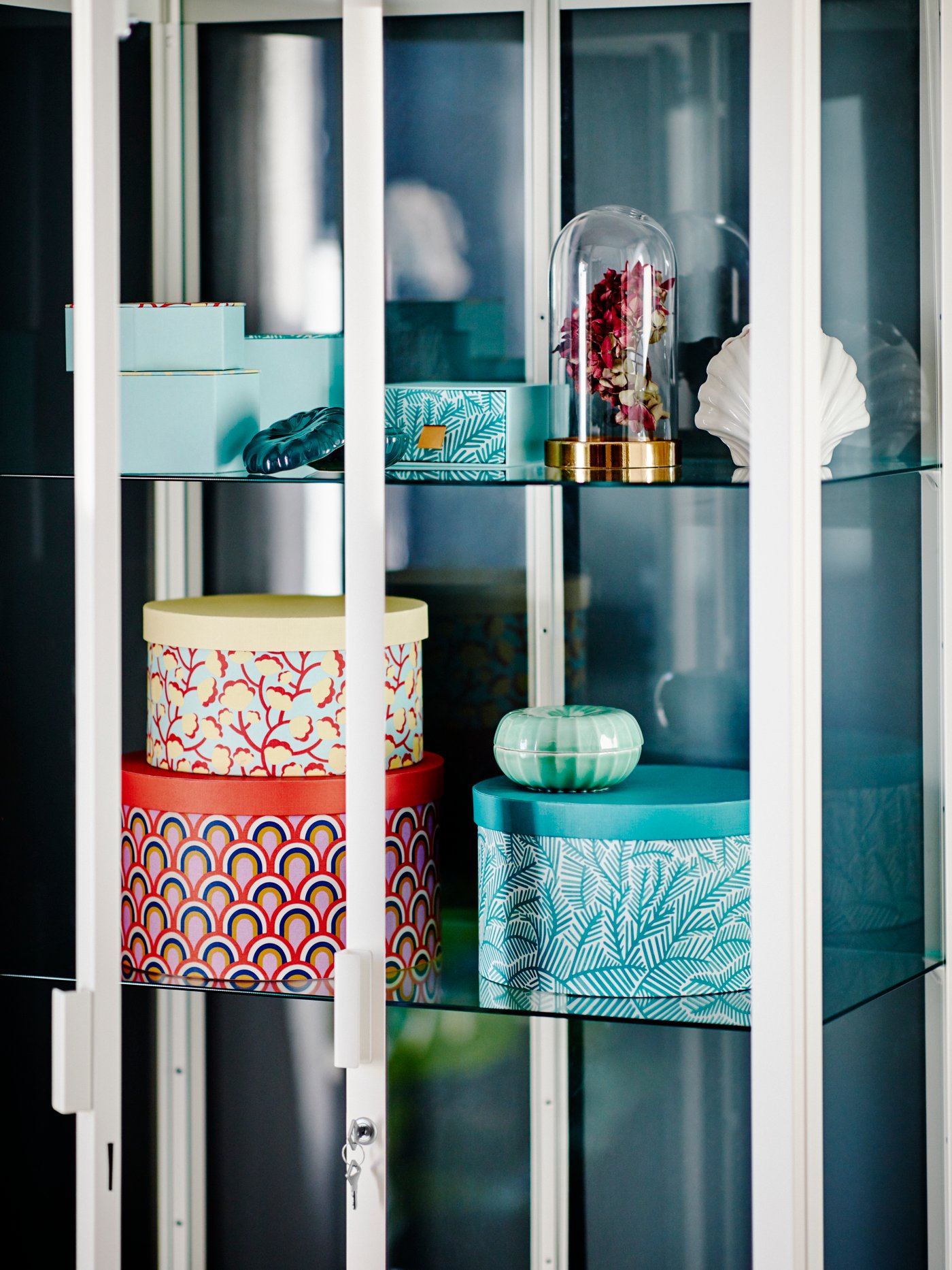 Una vetrina bianca con all'interno alcune scatole decorative colorate di diverse dimensioni e alcuni oggetti decorativi.