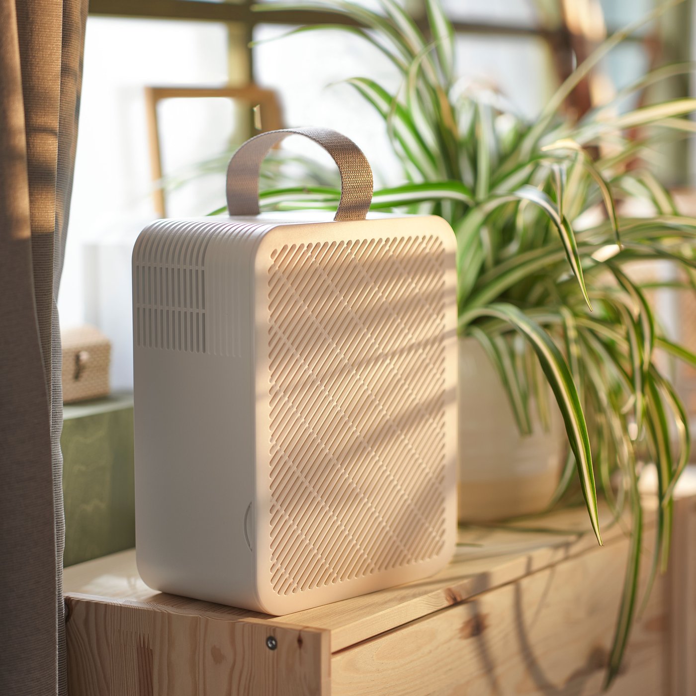 A pine RAST chest with 3 drawers in front of a window with a white UPPÅTVIND air purifier and a plant on top of it.