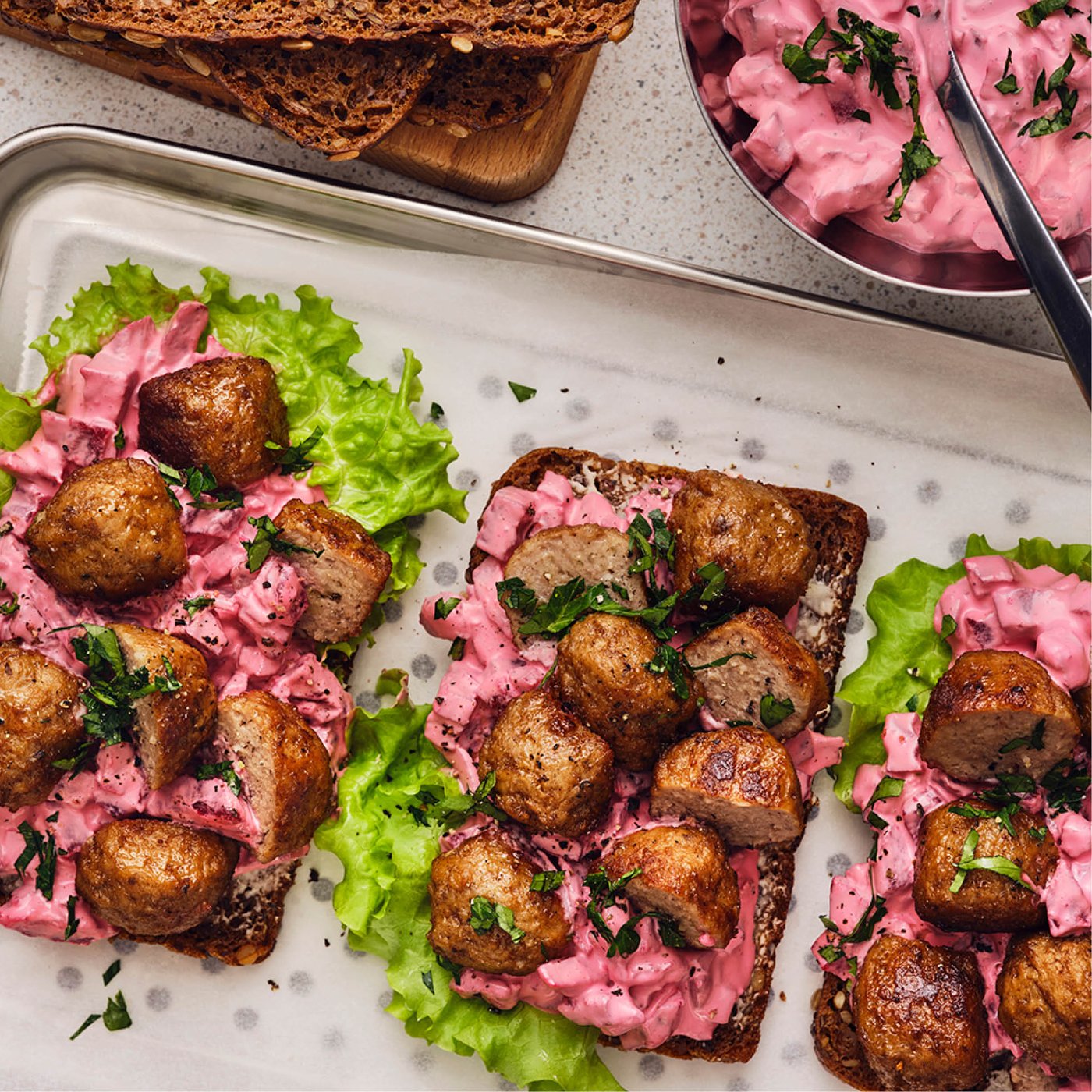 Open sandwiches met Zweedse gehaktballetjes, romige bietensalade en groene sla, geserveerd op een schaal met donker roggebrood.