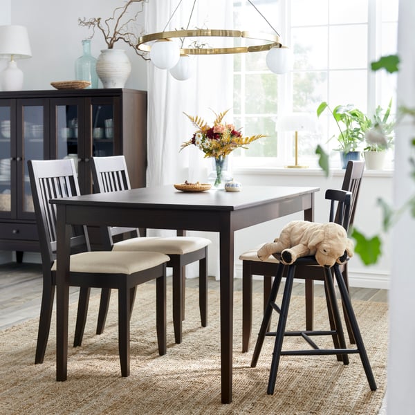 A dark brown NÄSINGE extendable table is set in a bright dining area with white chairs, flowers, and a pendant light.