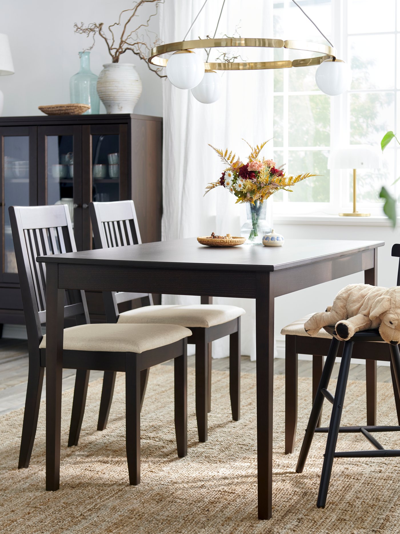 A dark brown NÄSINGE extendable table is set in a bright dining area with white chairs, flowers, and a pendant light.