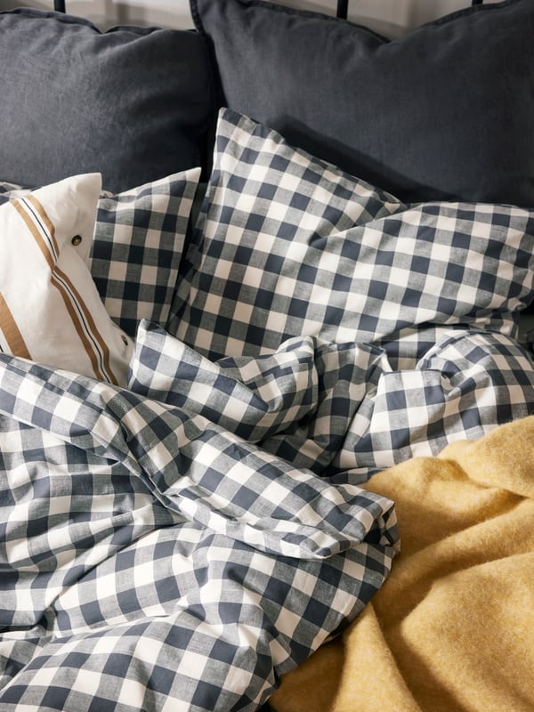 Close-up of bed with unmade bedding in yellow, grey and checkered grey and white.