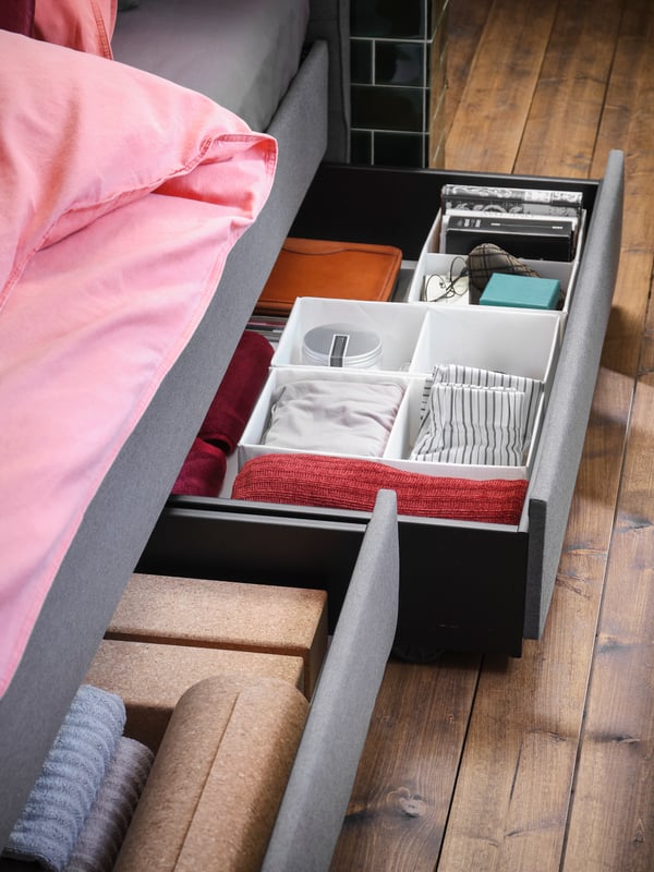 Caja organizadora de ropa con ruedas bajo una cama.