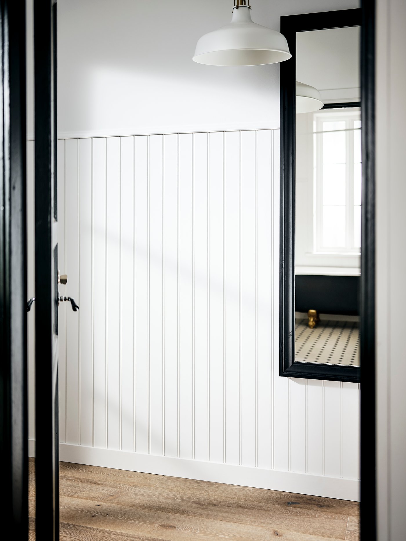 Une entrée blanche avec un miroir TOFTBYN dans un cadre noir fixé au mur et une suspension RANARP au-dessus.