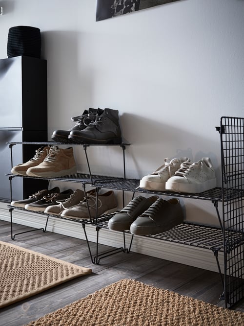 A modern hallway that features a shoe rack, a shoe cabinet with storage, a flatwoven rug, and a brown door mat.