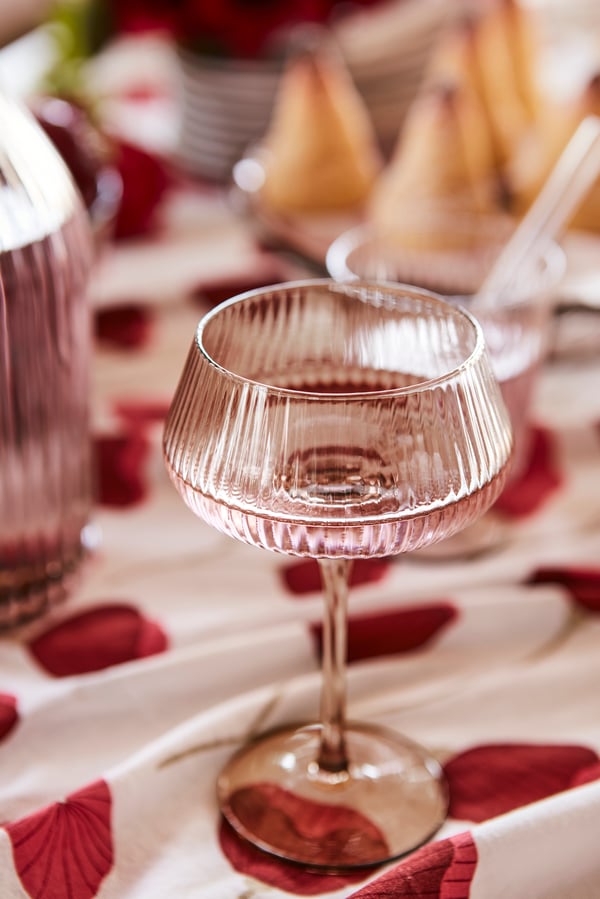 Närbild på ett rosa ANLEDNING champangeglas som står på en mönstrad duk i rött och vitt.