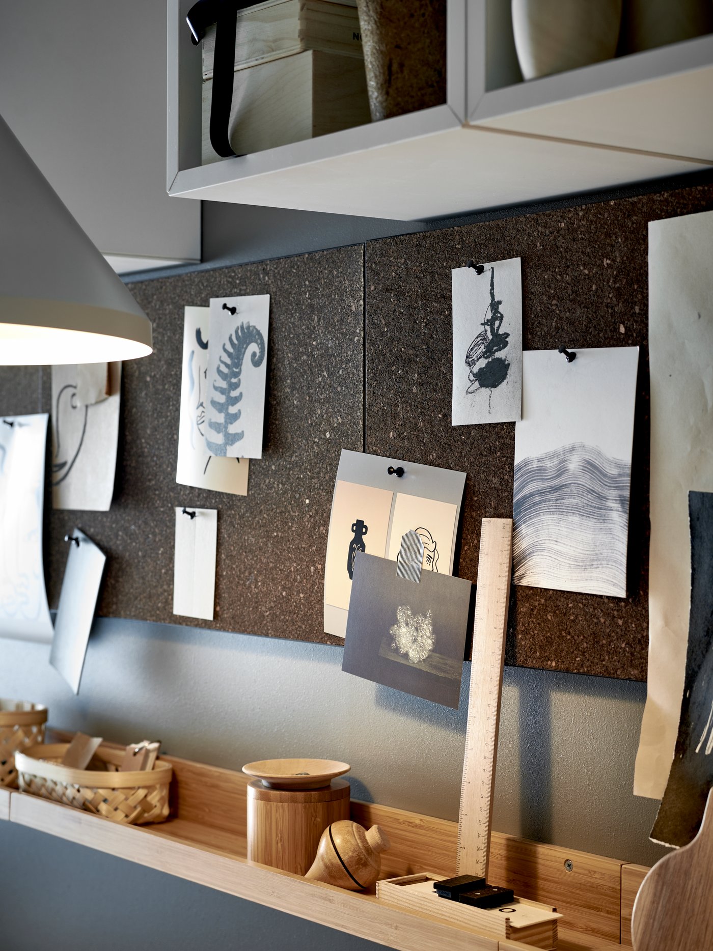 A row of dark brown SVENSÅS cork memo boards with art pinned to it, with shelving units above and a picture ledge below.