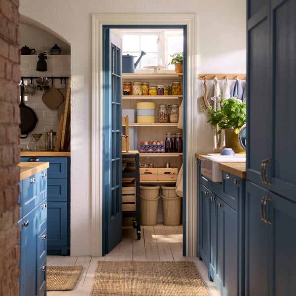 A METOD kitchen with LERHYTTAN blue fronts has a blue door that opens up to a pantry with several IVAR shelving units.