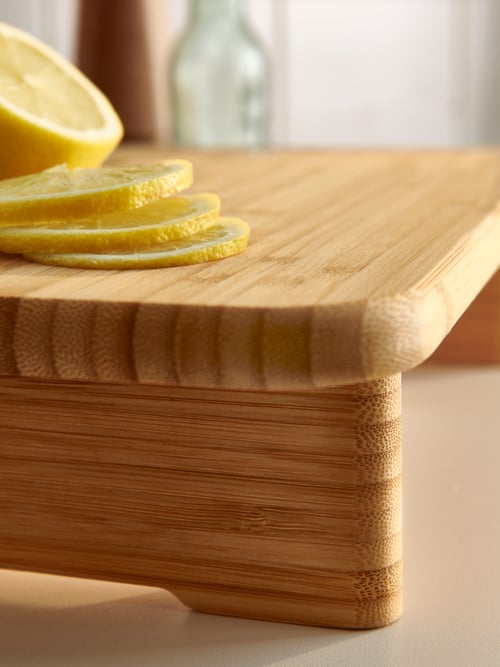 Close-up of the soft, rounded edges of the STOLTHET bamboo chopping board, with sliced lemons on top.