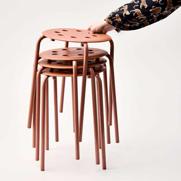 A person is holding a stack of red-brown MARIUS stools, showcasing their lightweight design and versatility.