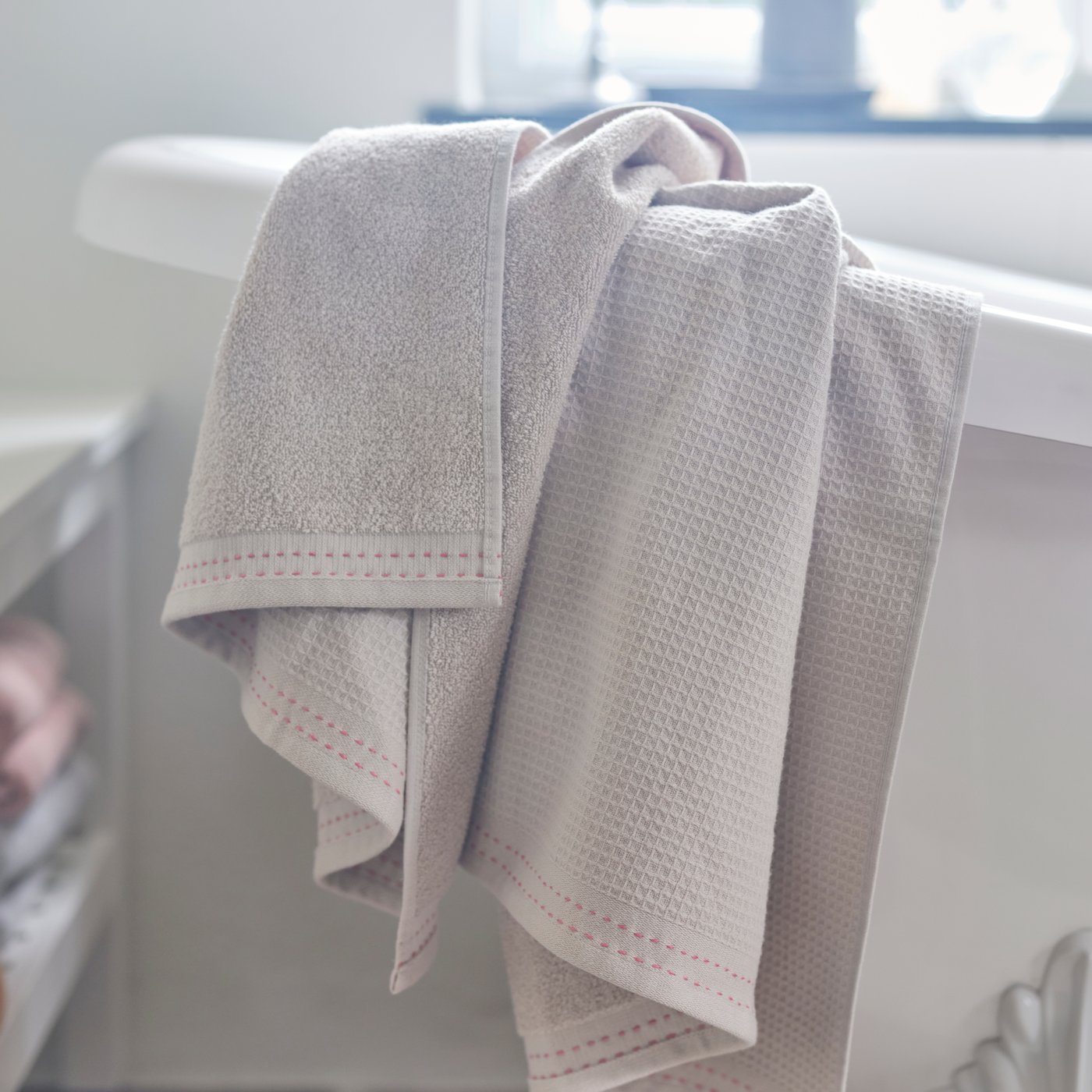 VÅRDANDE white cotton bath towel hanging over the edge of a bath in a bathroom.