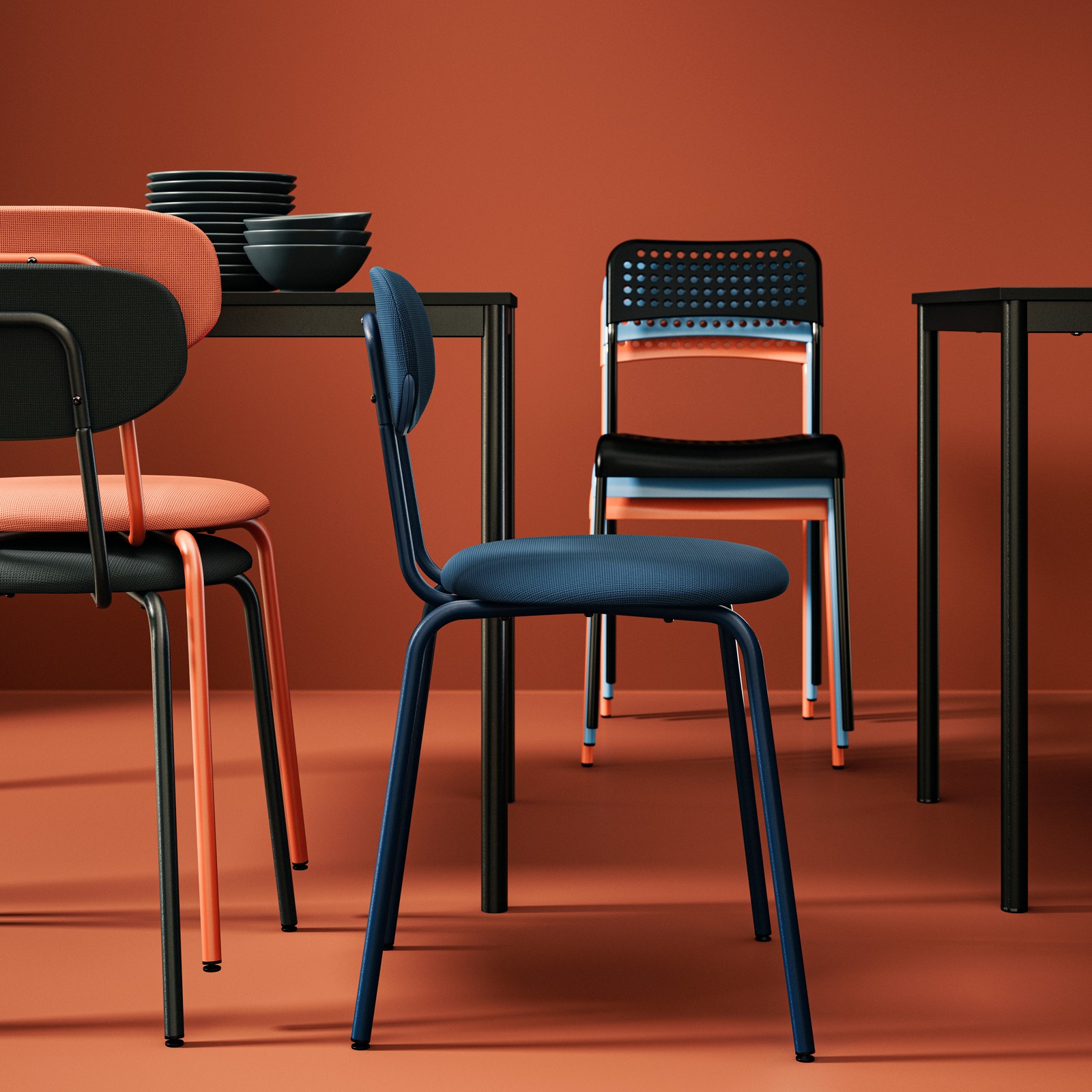 A SANDSBERG chair is standing next to some stacked chairs, all in different colours, set against a vibrant red background.