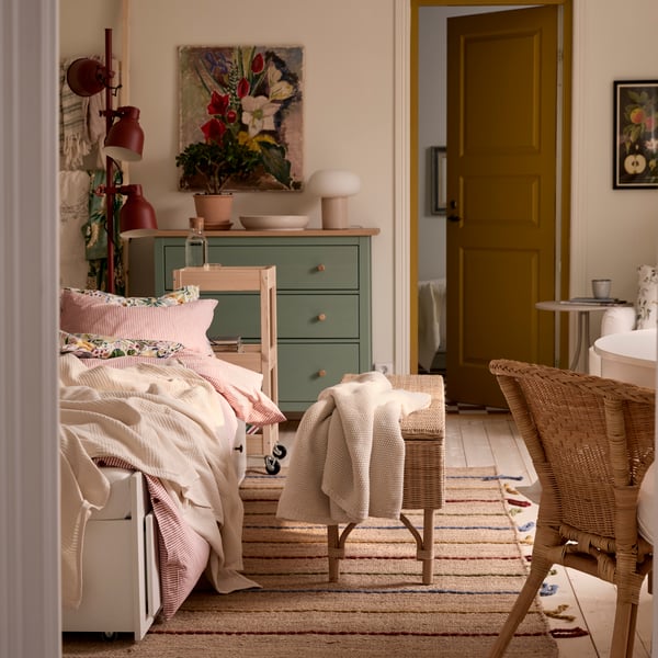 A one-bedroom apartment with HEMNES day-bed, a rattan chair in the foreground and a green HEMNES chest of drawers in the back.
