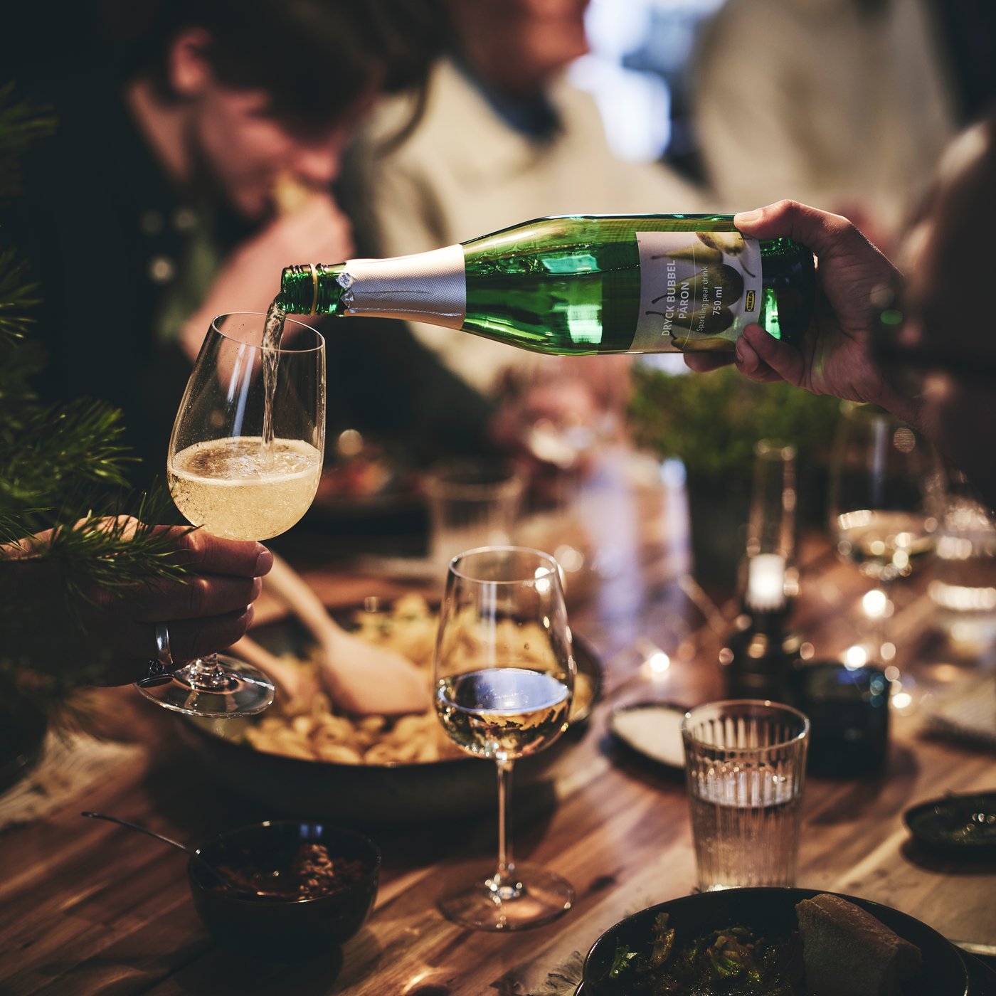Lors d’un souper festif, un invité verse une boisson pétillante dans le verre à vin d’un autre invité.