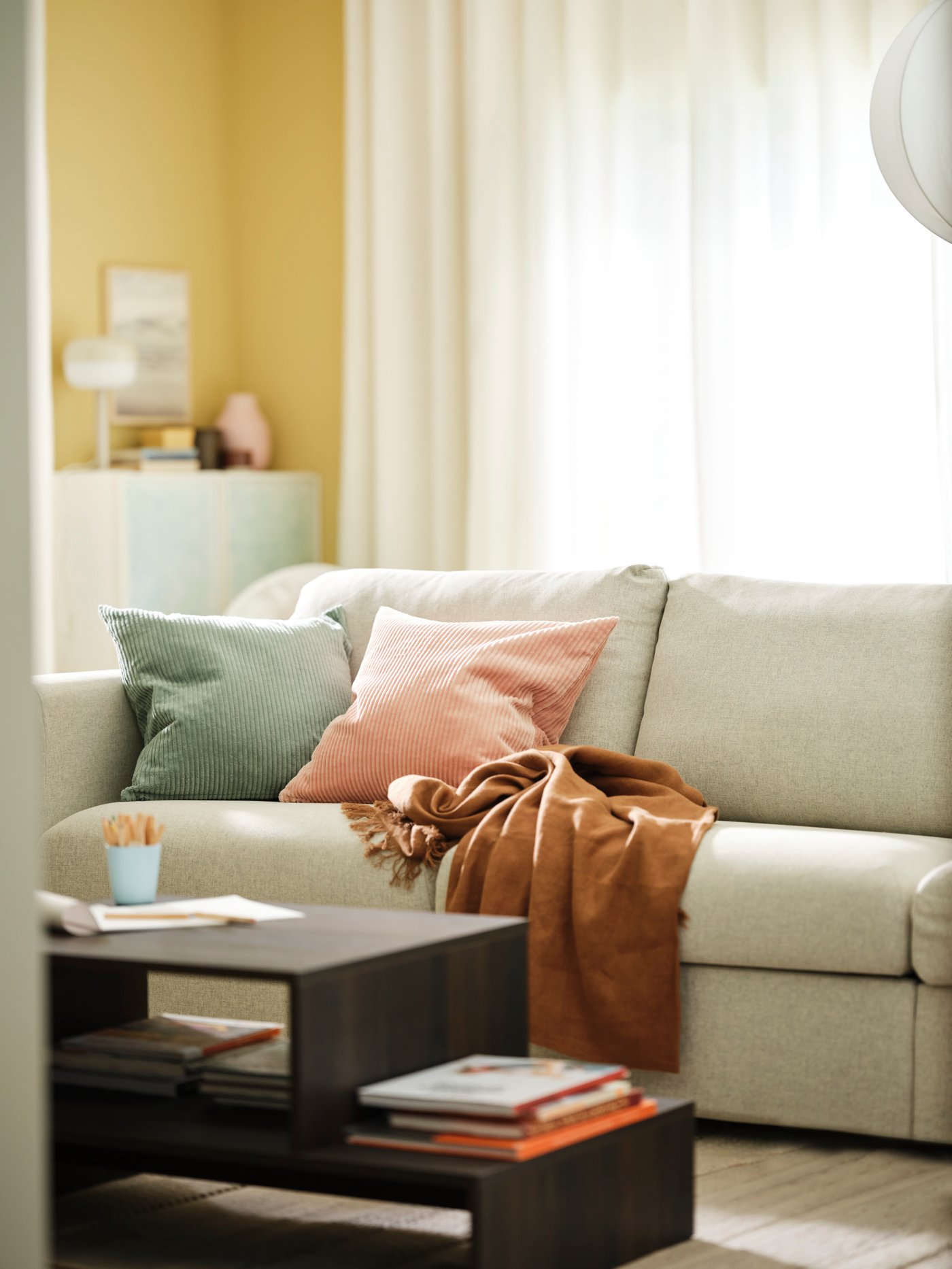 A beige VIMLE 2-seat sofa with cushions on it and a HOLMERUD coffee table are in a bright living room with yellow walls.