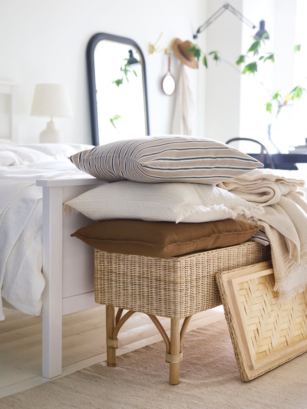 Cushions in LAGERPOPPEL, KORALLBUSKE and VALLKRASSIG covers piled top of a rattan TOLKNING bench with storage.