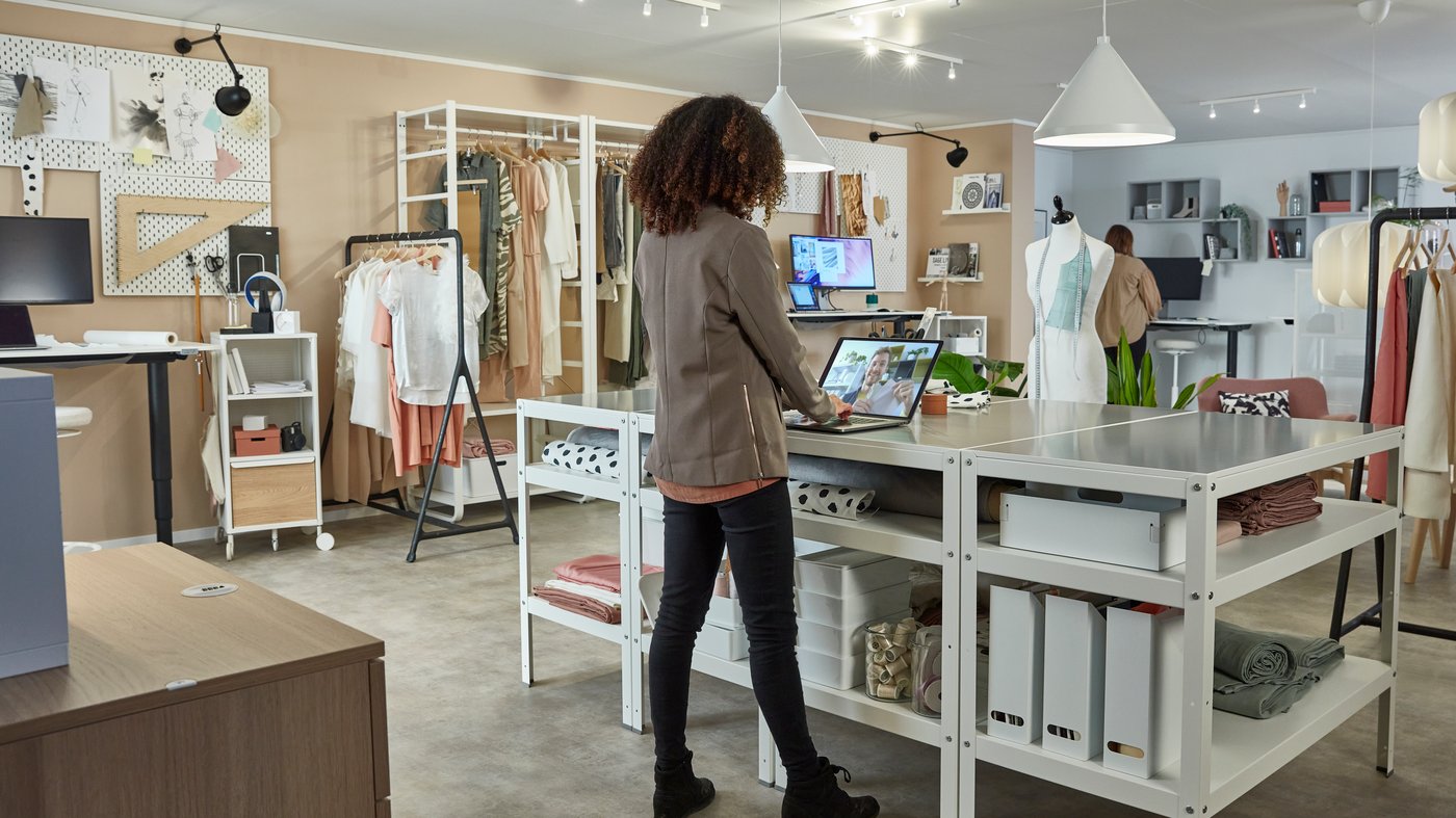 A woman stands at a desk among IKEA furniture with her computer and has a video call.