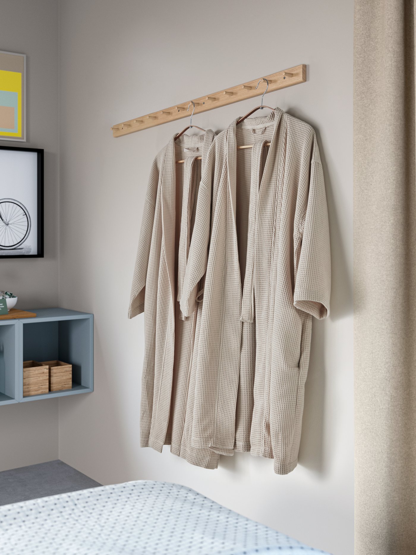 Två våffelmönster från ROCKÅN badrockar hänger på HÖVOLM-ställ i ett hotellrum med ljusgråblå EKET-skåp.