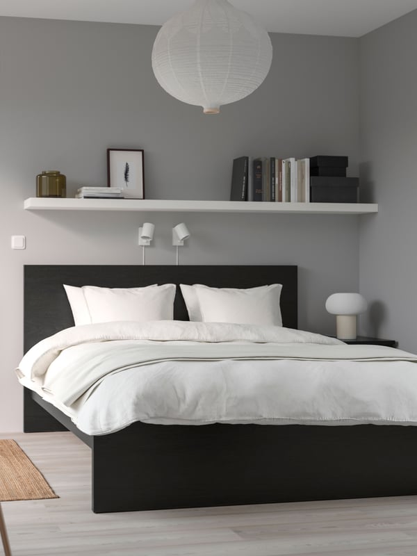 Una cama con ropa de cama blanca y una estantería llena de libros sobre ella.
