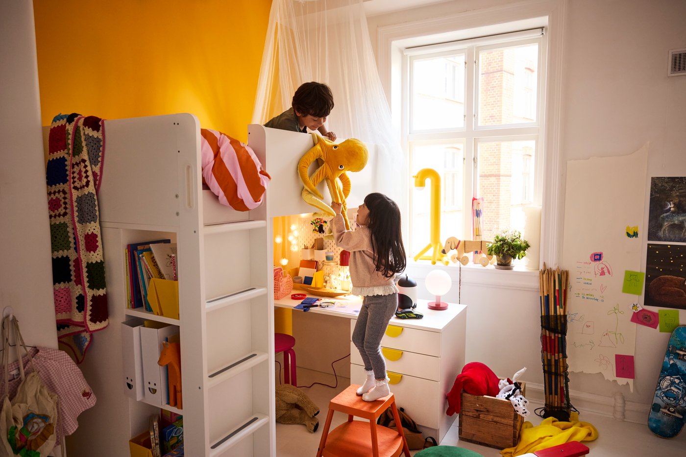 Two children in a children's room are playing with a soft toy, one is up in a bunk bed and the other is down on the floor.