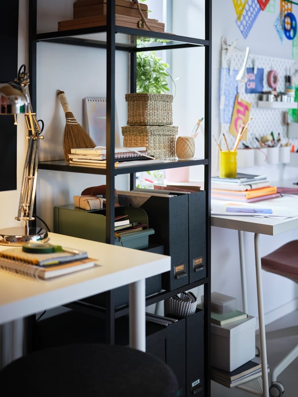 By a desk with a white LAGKAPTEN tabletop lit by a FORSÅ work lamp, stands a high, black-brown VITTSJÖ shelving unit.