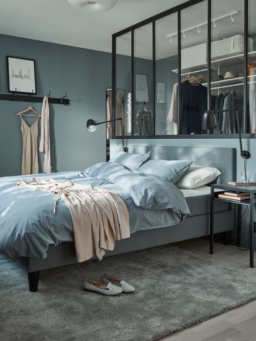 Bedroom featuring a divan bed with headboard covered by a blue duvet cover with 2 pillowcases, placed over a rug low pile.