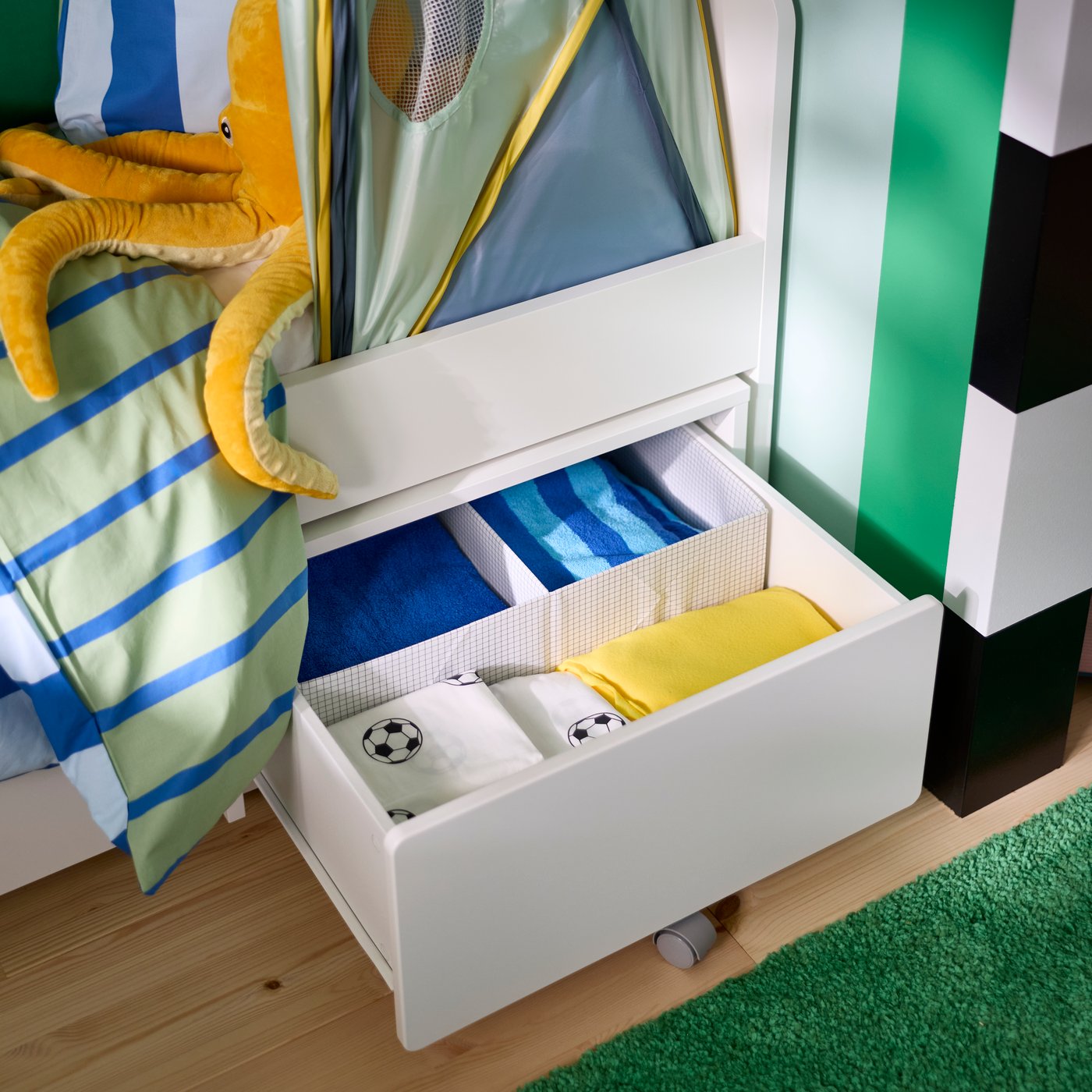 A SLÄKT storage box with castors pulled out from under a children’s bed, filled with bedding.