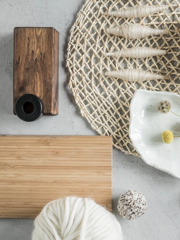 APTITLIG bamboo chopping board on a white marble surface together with a coarsely woven place mat and four spindles of yarn.
