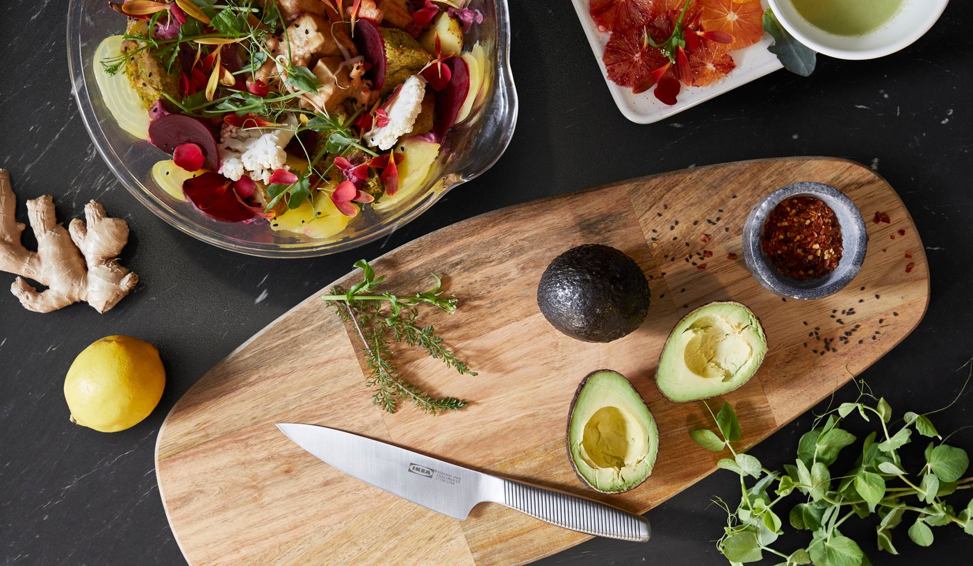 Fresh ingredients and a salad arranged on a dark countertop with a cutting board and knife.