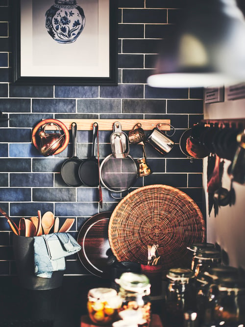 Gros plan sur un mur de cuisine moderne recouvert de carreaux noirs, une patère en chêne massif à 6 boutons fixée au mur et des ustensiles.