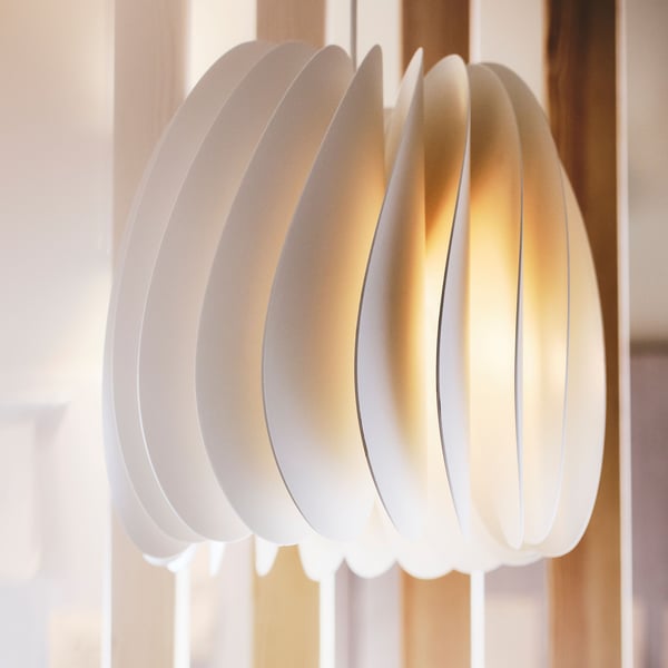 A soft yellow light diffuses from within a white SKYMNINGEN pendant lamp.