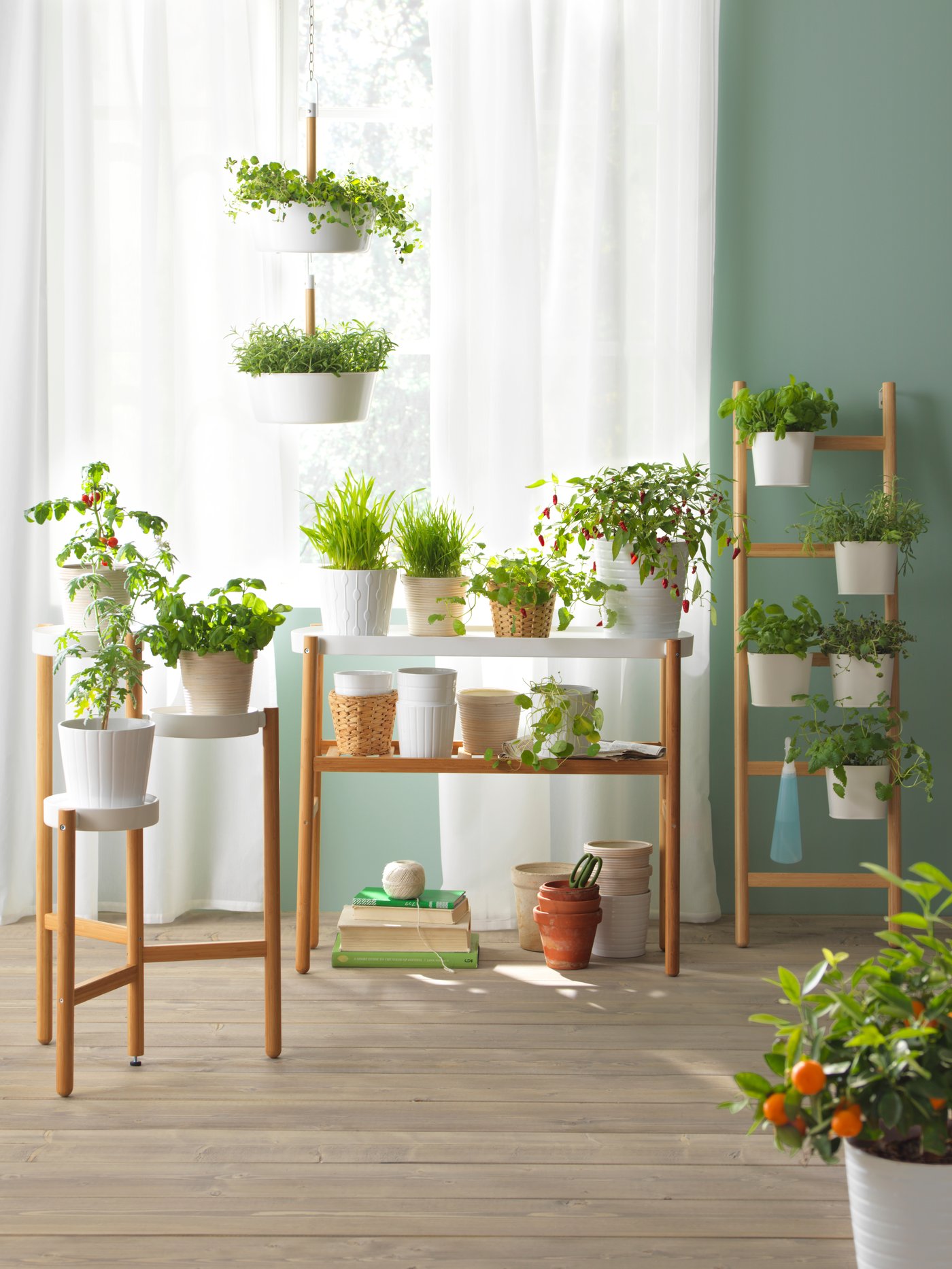 Několik stojanů SATSUMAS v provedení bambus/bílá uvnitř světlé místnosti se spoustou pokojových zelených rostlin.