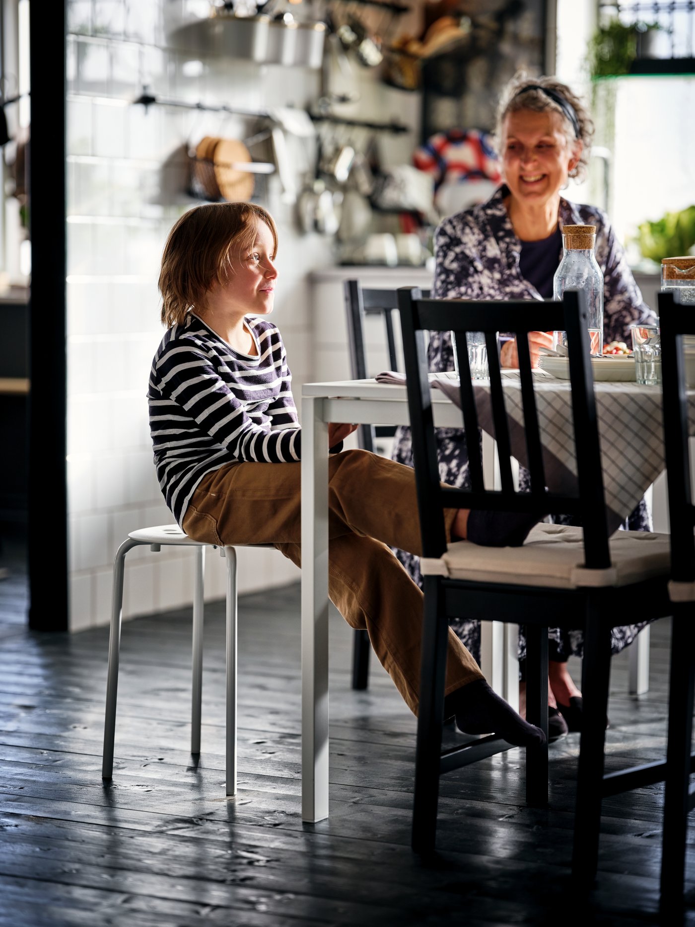 A dining area with a boy on a white MARIUS stool and a woman on a brown-black STEFAN chair, by two white MELLTORP tables.