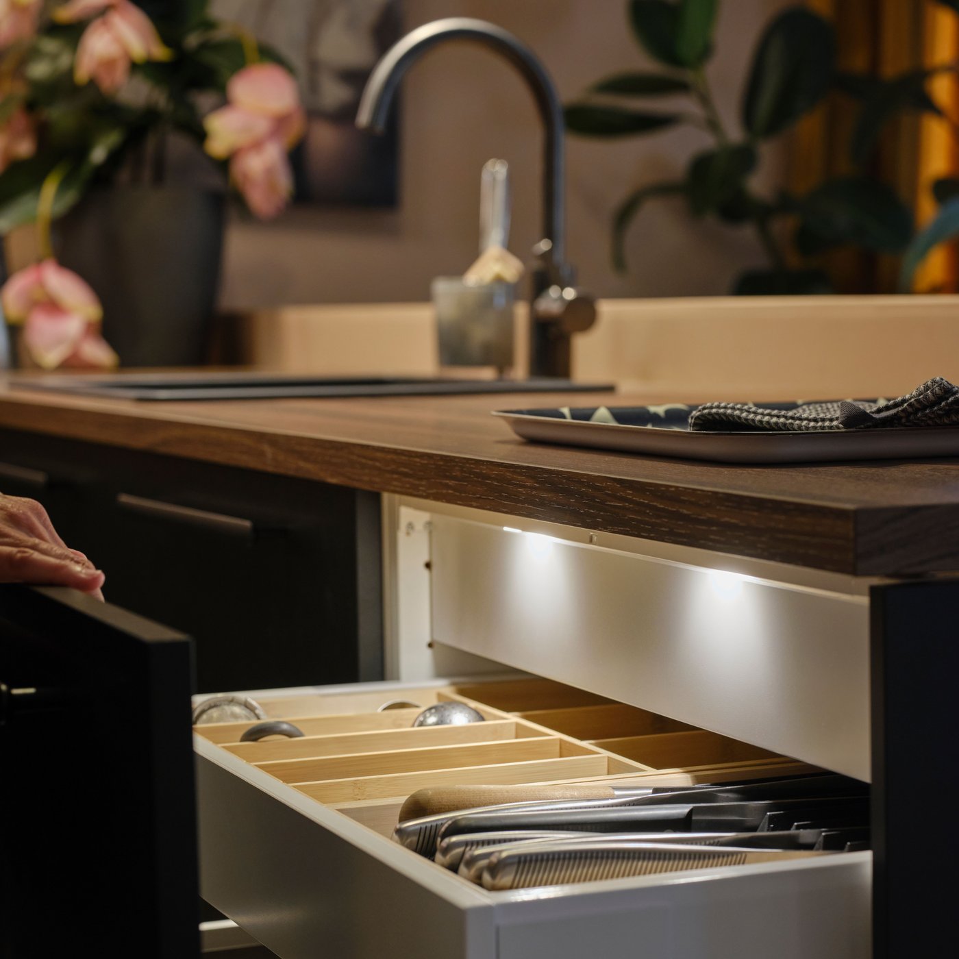 Une personne ouvre un tiroir de cuisine avec une façade anthracite mat, montrant l'éclairage de tiroir de cuisine MITTLED LED avec capteur à l'intérieur.
