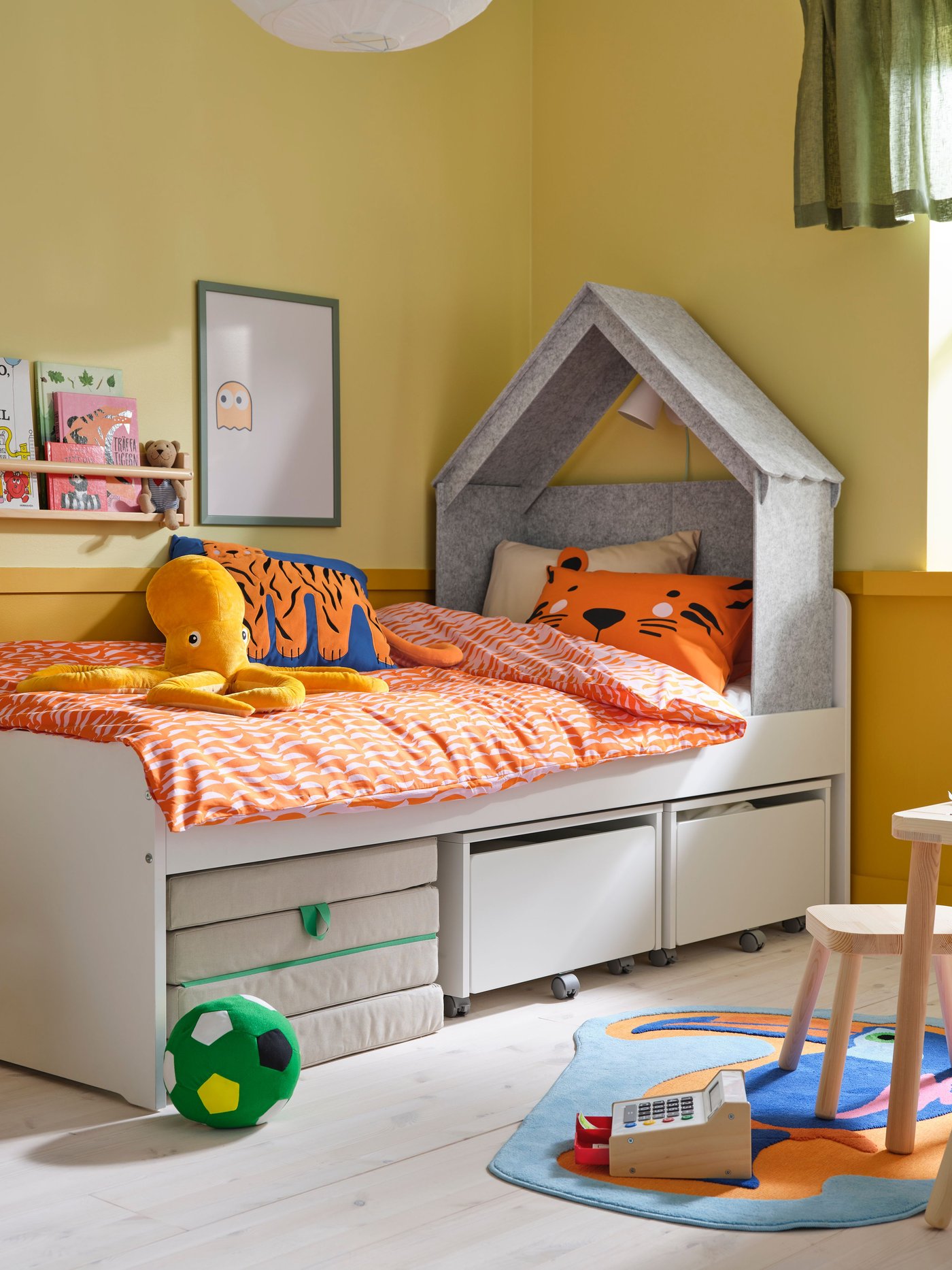 Kinderbett mit grauem Hausaufsatz und orange gemusterter Bettwäsche. Darunter Schubladen zur Aufbewahrung.